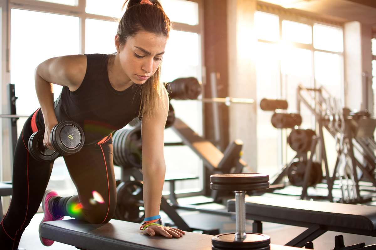 A woman works out with handheld weights in a gym. Working out with CBD can help promote muscle gain and increase stamina for exercise.