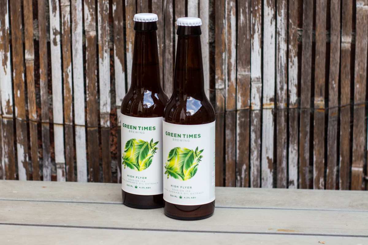 Two bottles of "High Flyer" CBD Beer sit on a table in front of a worn bamboo backdrop. The UK's new CBD beer is exciting tastebuds as it relaxes drinkers.
