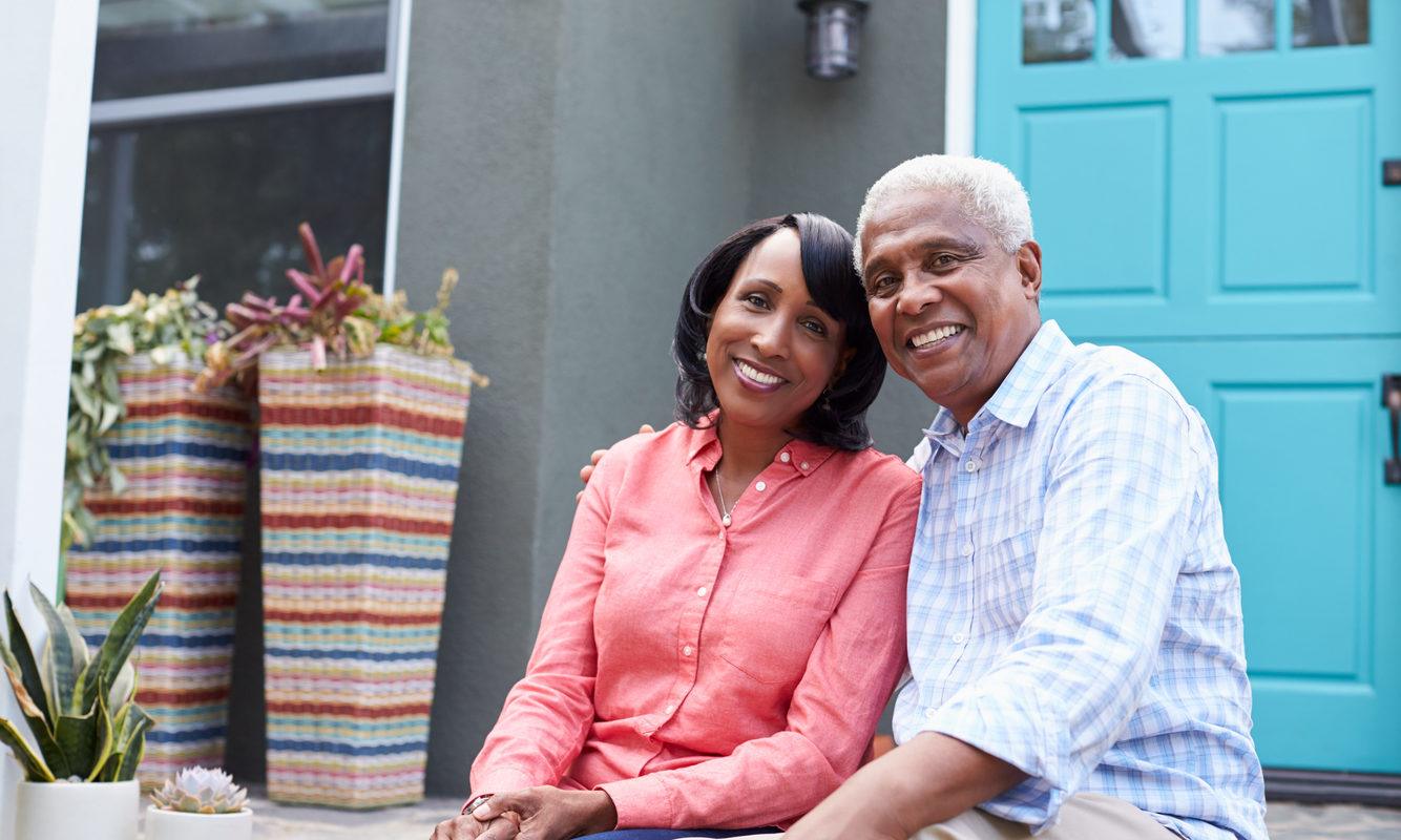 A woman and man, a senior citizen couple, sit outside their home. He has his arm around her. There are numerous benefits of CBD for senior citizens, from reducing inflammation to easing anxiety.