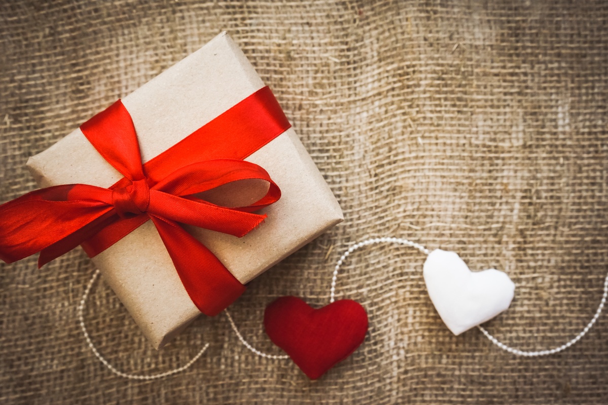 A gift wrapped with a red ribbon and decorated with hearts on a string, sitting on a fabric background. Our Valentine's Day CBD Gift Guide can make your holiday more relaxed, healthier, and more romantic too.