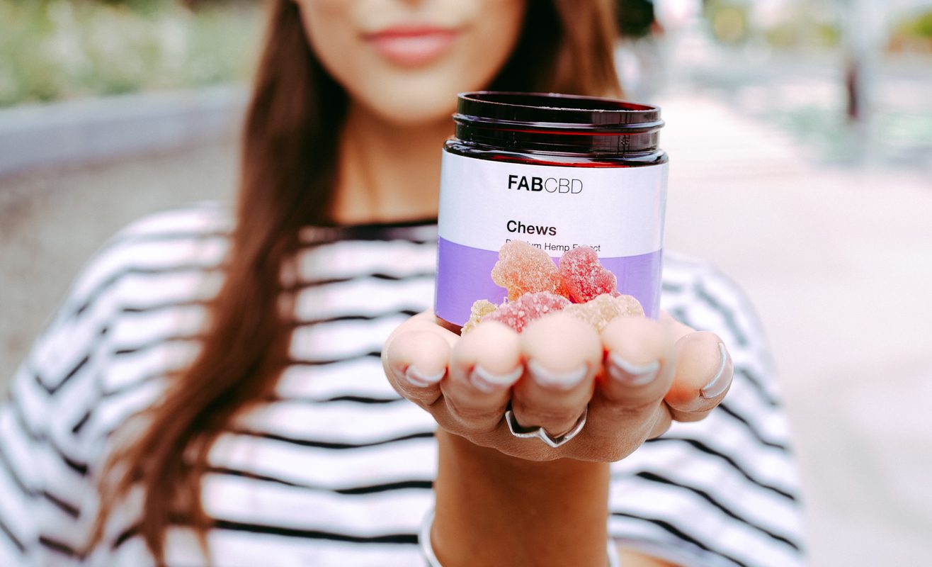 A woman holds Fab CBD Chews in her outstretched hand, including the jar and individual gummies.