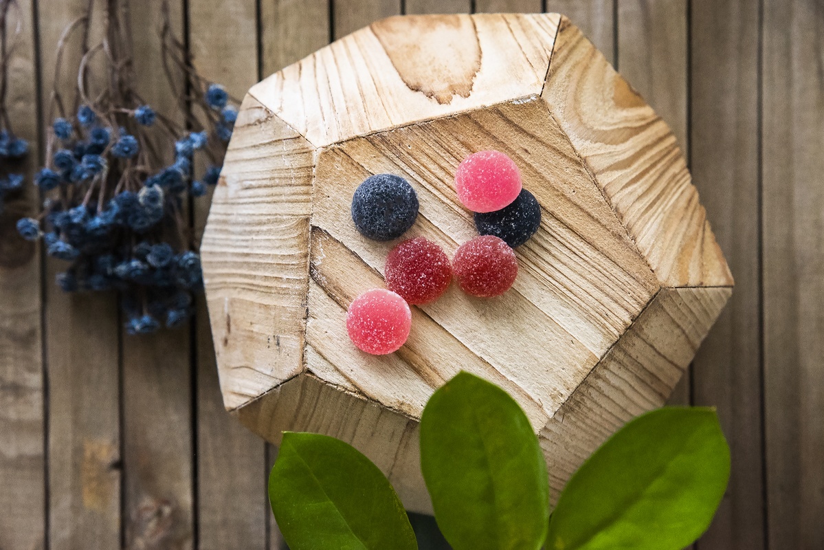 Photo: Wana Wellness Hemp Gummies in Berry Medley flavoers, posed on a wooden display stand, decorated with flowers and leaves.