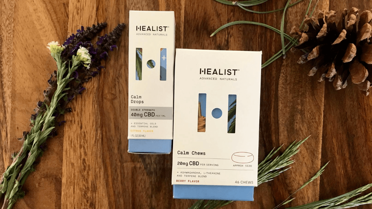 The box and CBD product label for two Healist Naturals produts, arranged with a pine cone and herbs.