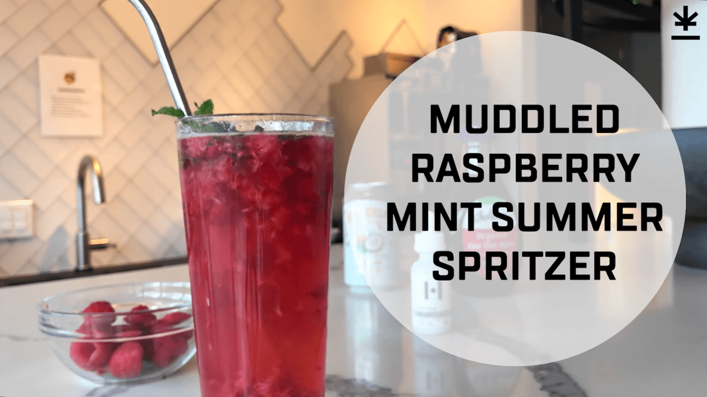 A glass of raspberry CBD spritzer with a metal straw in it, garnished with a mint leaf. Text reads "Muddled Raspberry Mint Summer Spritzer."